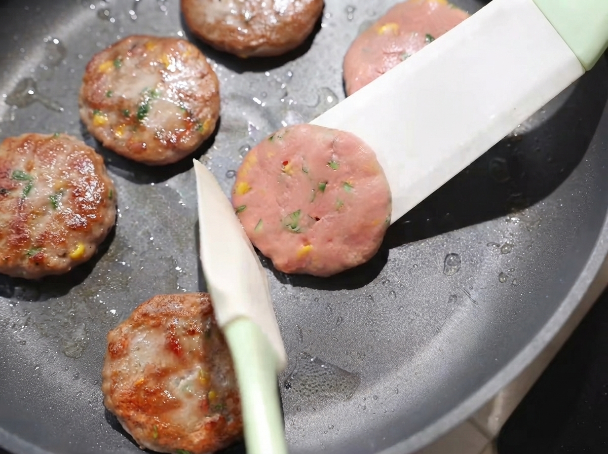 Polpette girate nella padella con una spatola, che mostrano le superfici dorate cotte a fuoco basso.