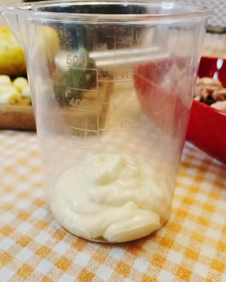 Un cucchiaio di maionese densa sul fondo di un misurino di plastica trasparente.