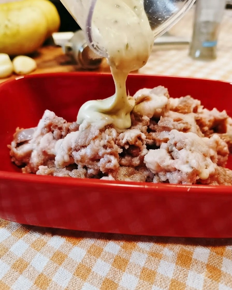 La salsa viene versata da un contenitore trasparente in una ciotola rossa piena di manzo macinato condito.