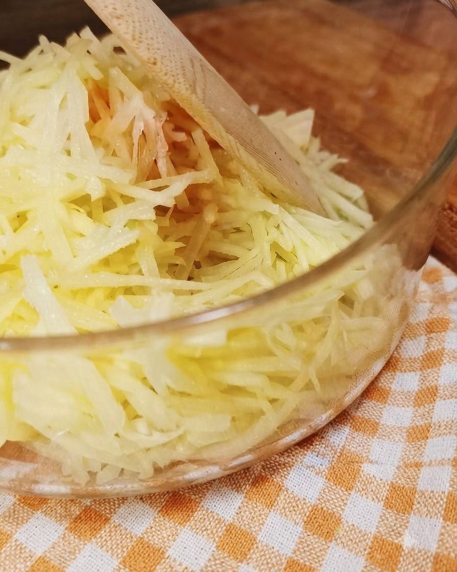 Patate fresche grattugiate allinterno di un contenitore di vetro trasparente con un utensile di legno.