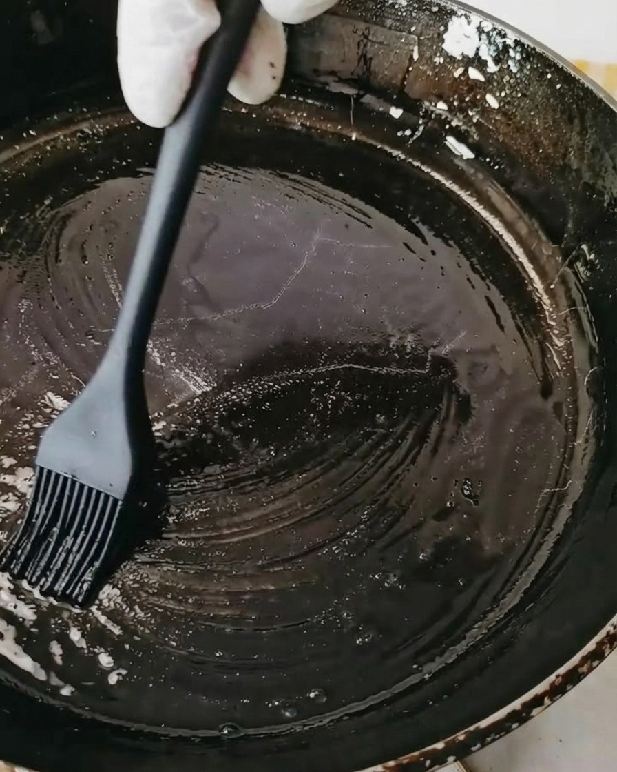 Una padella nera spennellata con olio utilizzando un pennello da cucina in silicone nero.