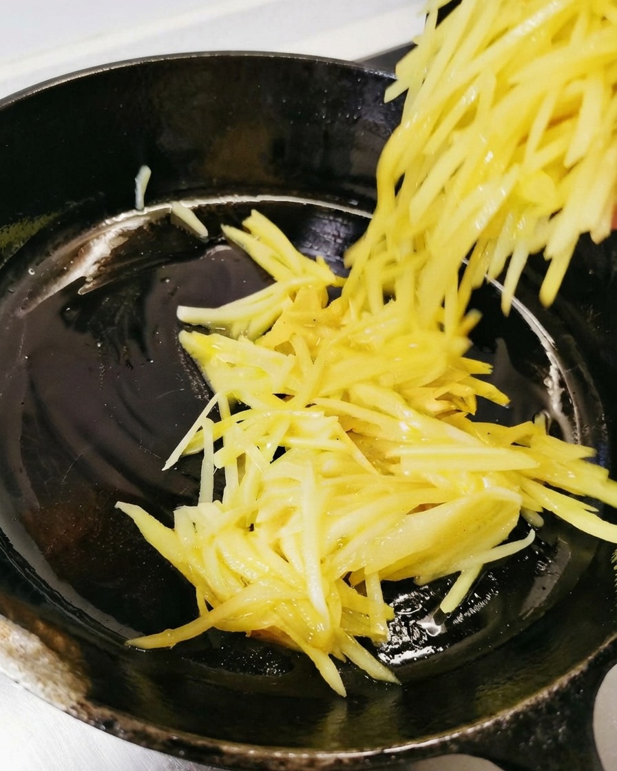 Patate grattugiate versate e distribuite nella padella nera unta.