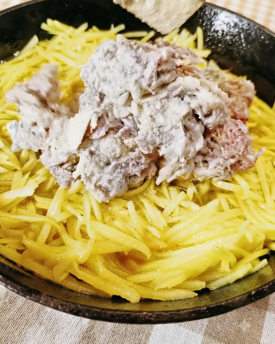 Manzo macinato condito accumulato sopra uno strato giallo di patate grattugiate allinterno di una padella.