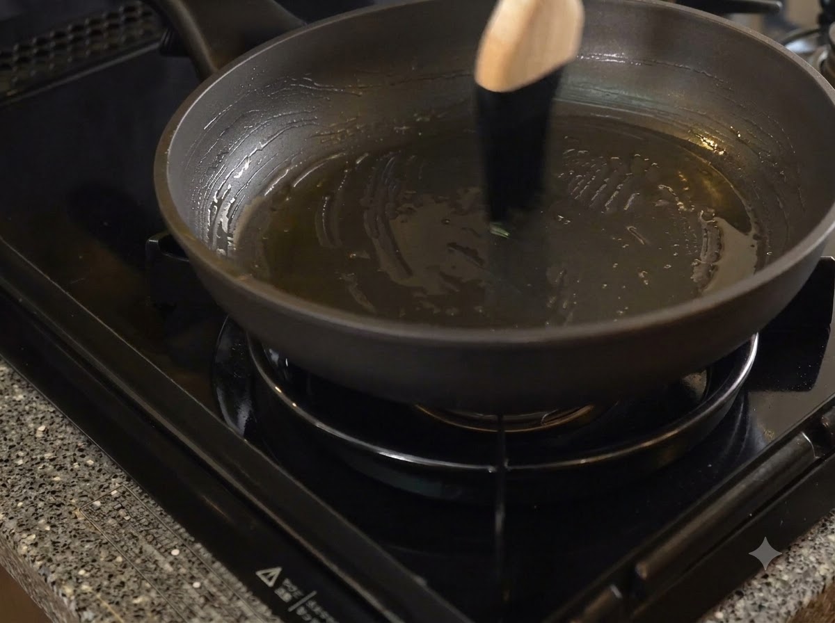 Una padella antiaderente scura spennellata con dello strutto usando un pennello da cucina con manico in legno.