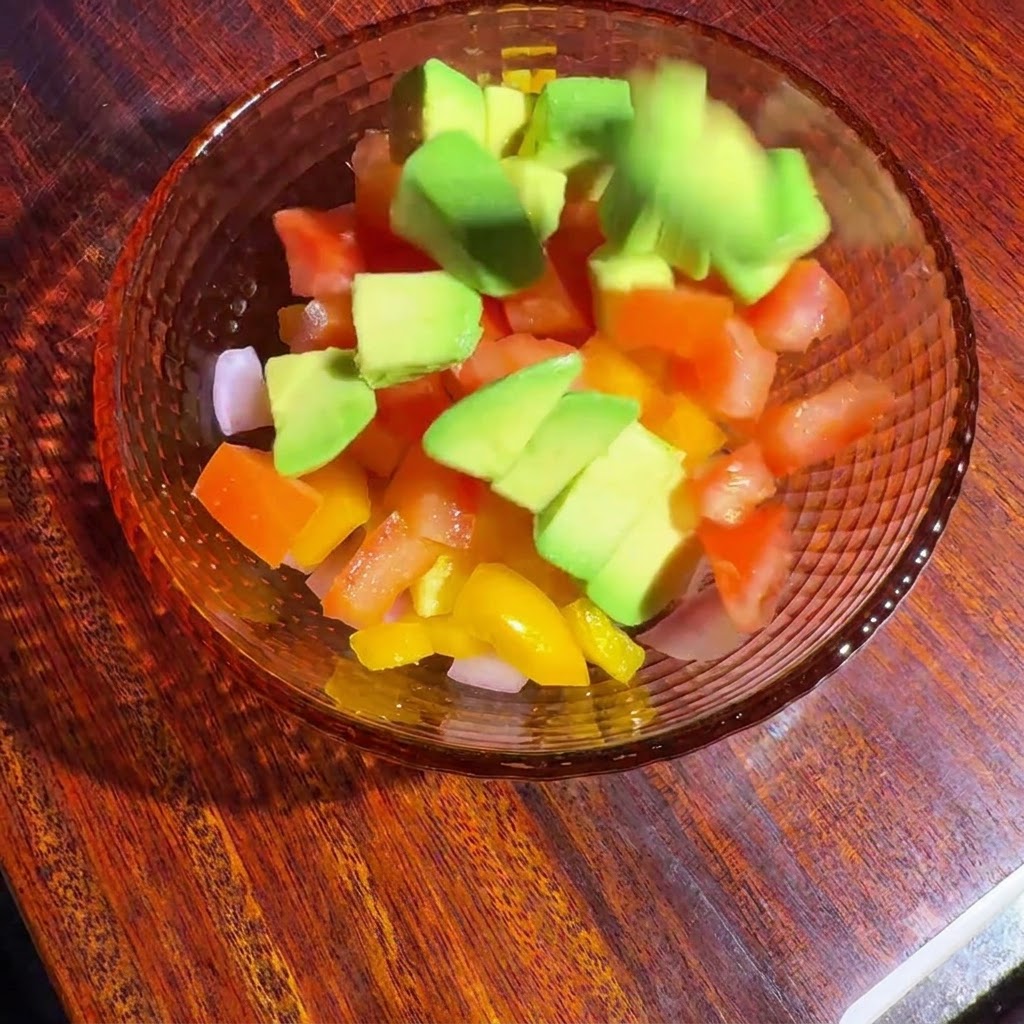 Verdure a dadini e avocado in una ciotola di vetro che vengono mescolati con il condimento.