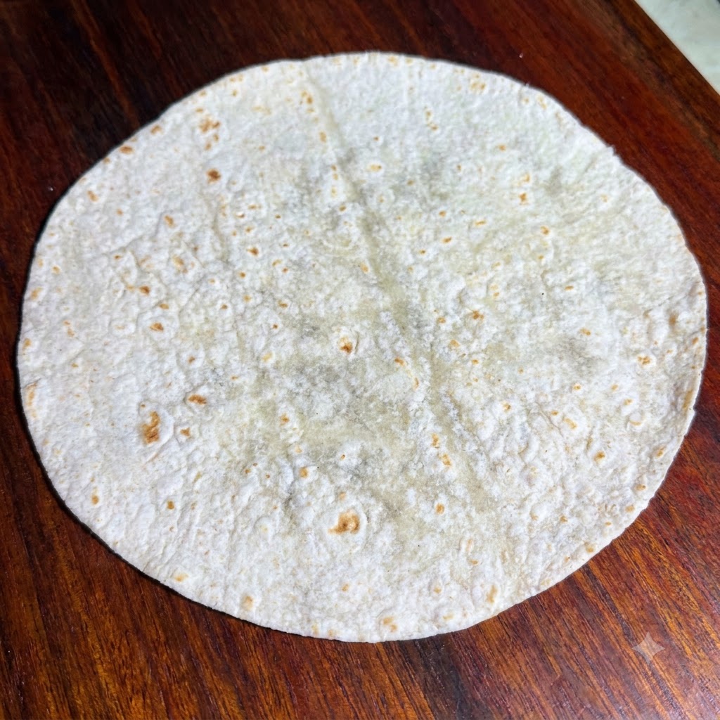 Foglie di lattuga verde fresca disposte ordinatamente sopra una tortilla integrale tonda e piatta.