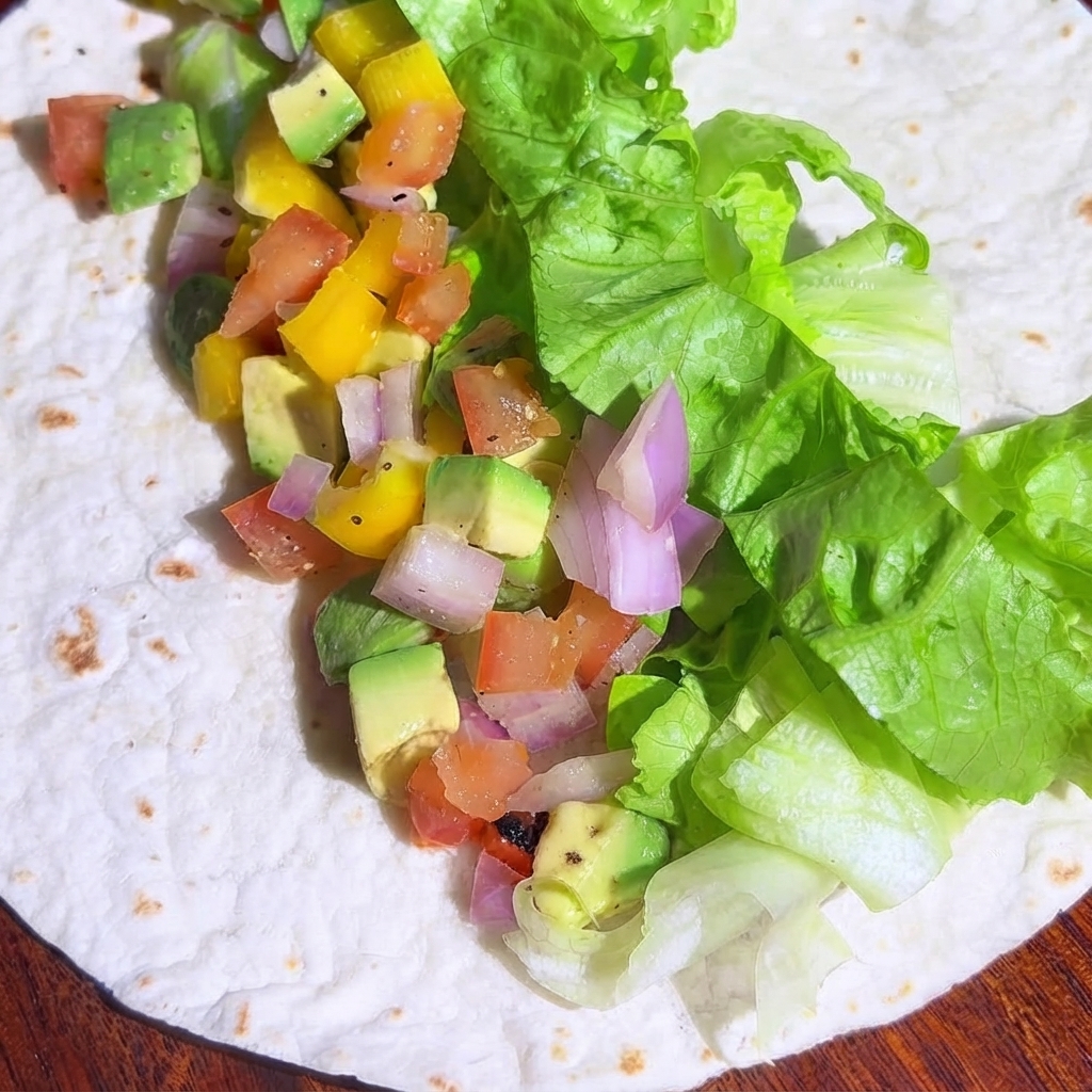 Pezzi di pollo cotto a dadini distribuiti sul ripieno di verdure sulla tortilla.