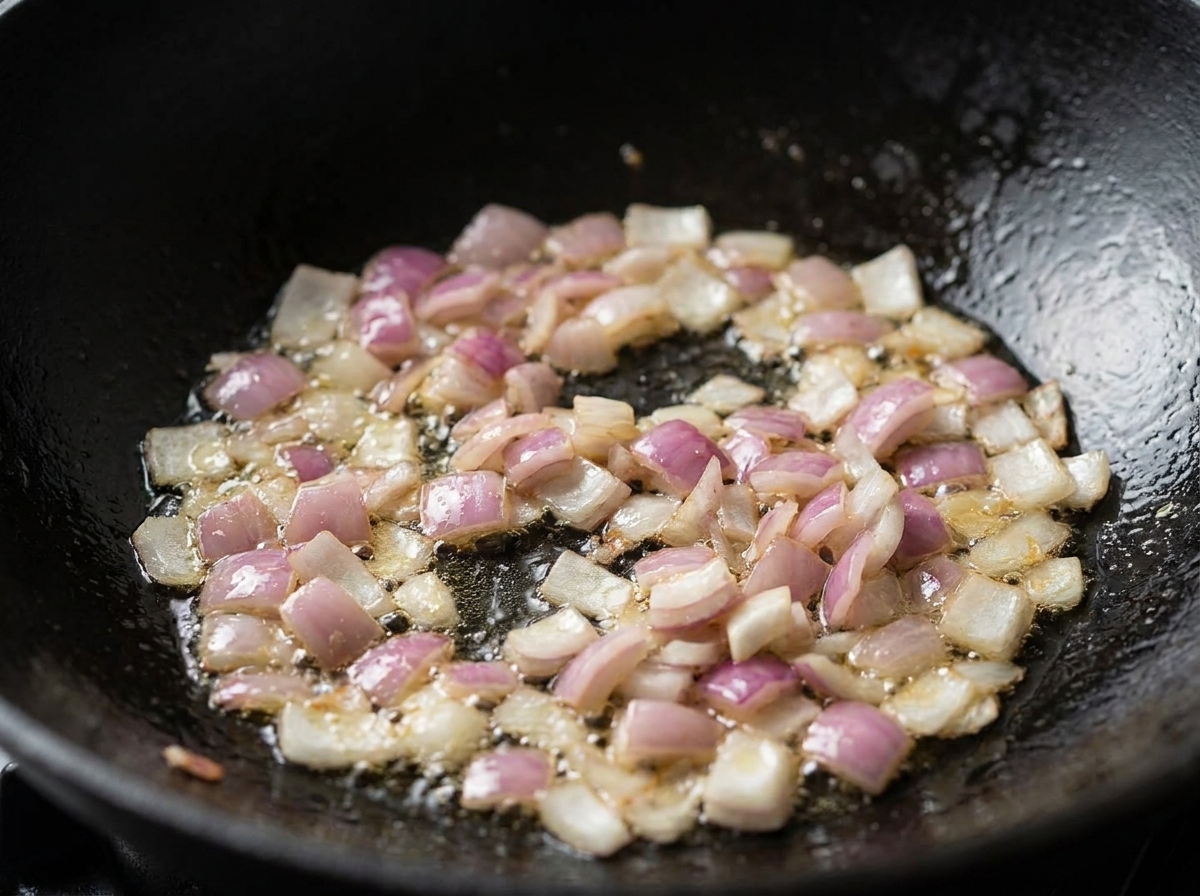 Cipolle rosse a cubetti e pancetta che sfrigolano nellolio allinterno di un wok nero.
