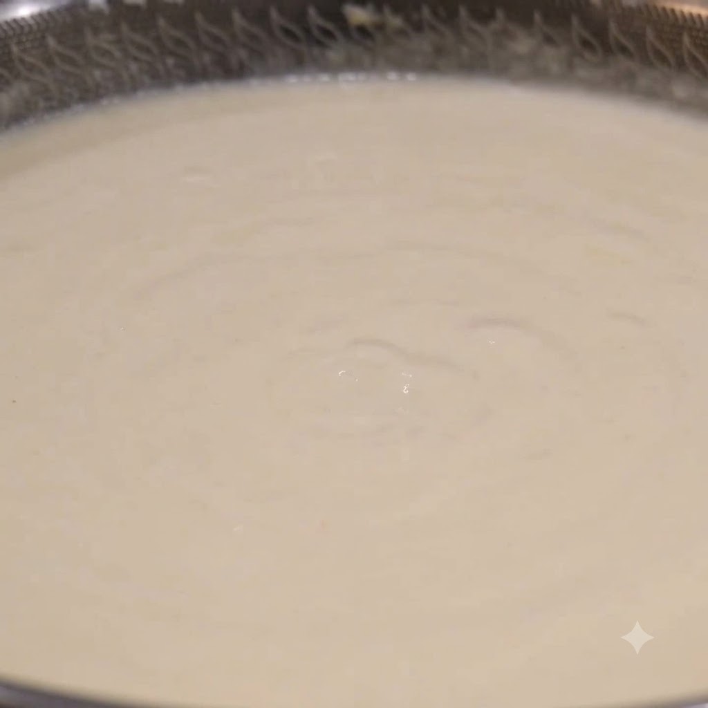 Un mestolo che raccoglie zuppa di vongole bianca e cremosa da un wok in ebollizione.