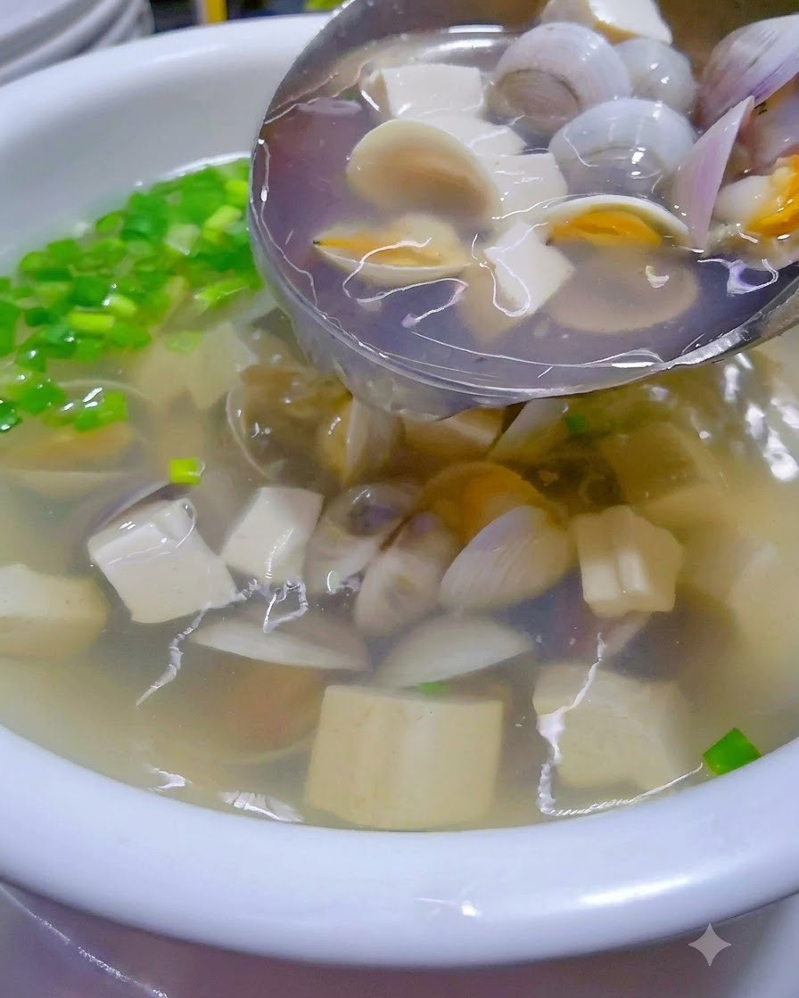 Zuppa calda di vongole e tofu versata da un wok in una ciotola da portata guarnita.