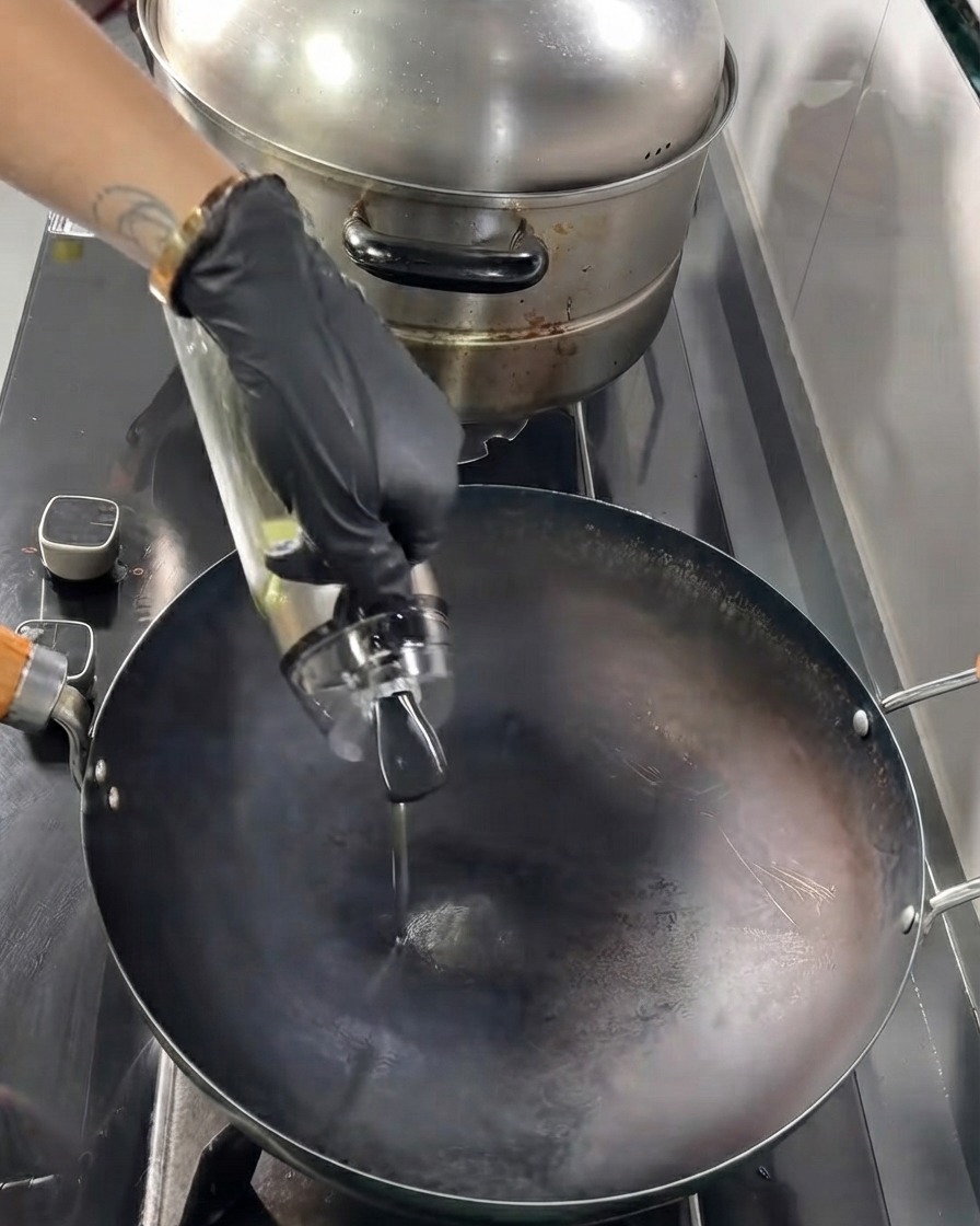 Olio da cucina versato da una bottiglia di vetro in un wok nero caldo.