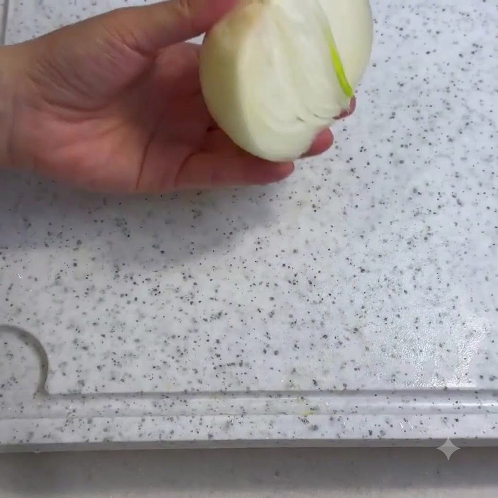 Una cipolla tagliata a fette su un tagliere bianco con un coltello.