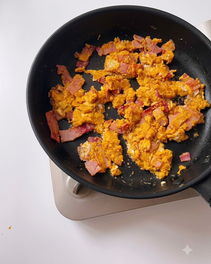 Acqua versata da un misurino in una padella nera con uovo salato e pancetta.
