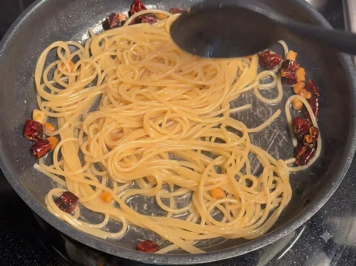 Acqua della pasta mescolata agli spaghetti e al maiale in padella.