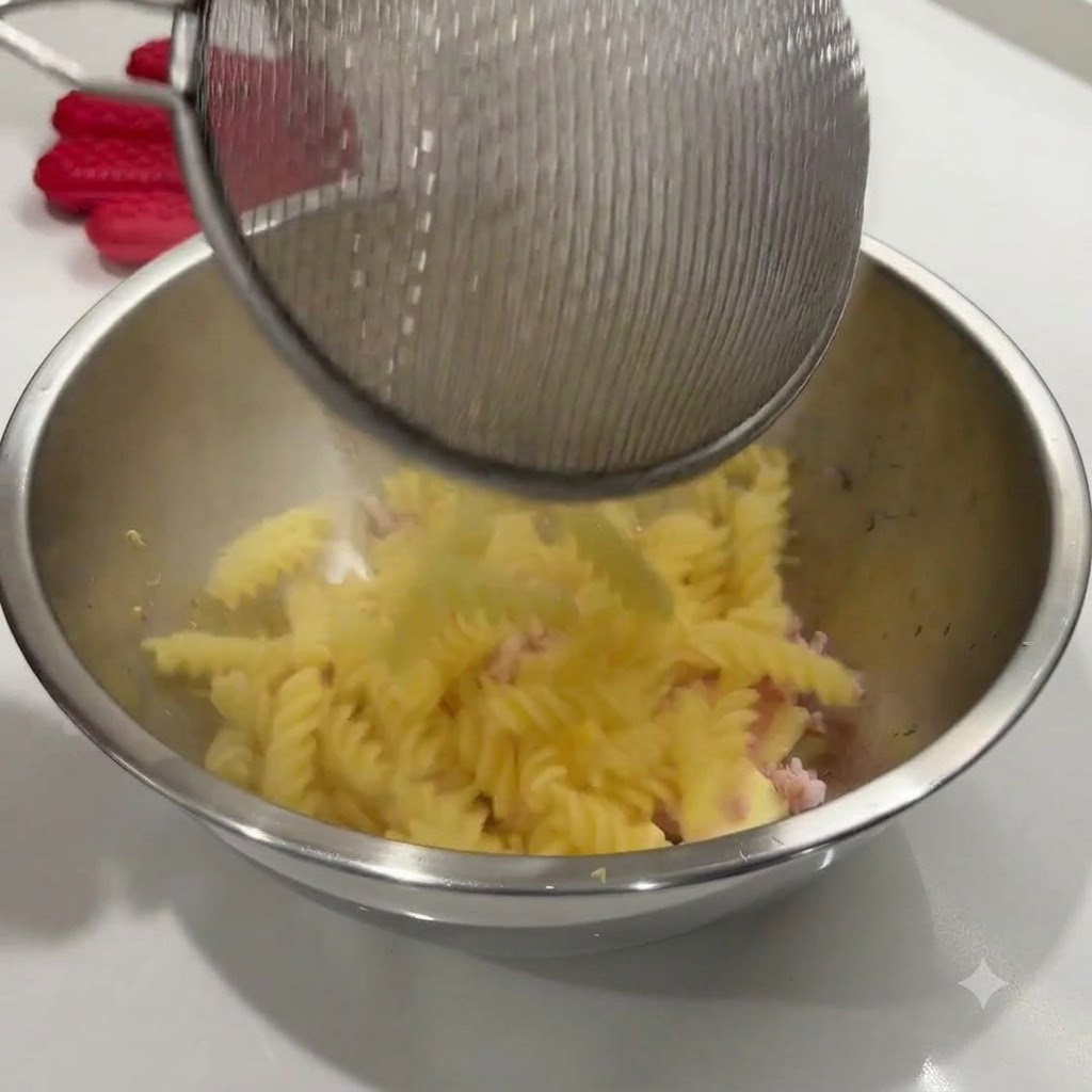 Pasta a spirale cotta versata da un colino in una ciotola in acciaio inossidabile con gli altri ingredienti.