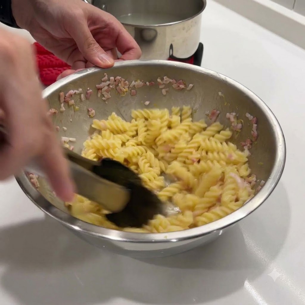Mescolare pasta a spirale calda e burro in una ciotola di metallo usando pinze nere.