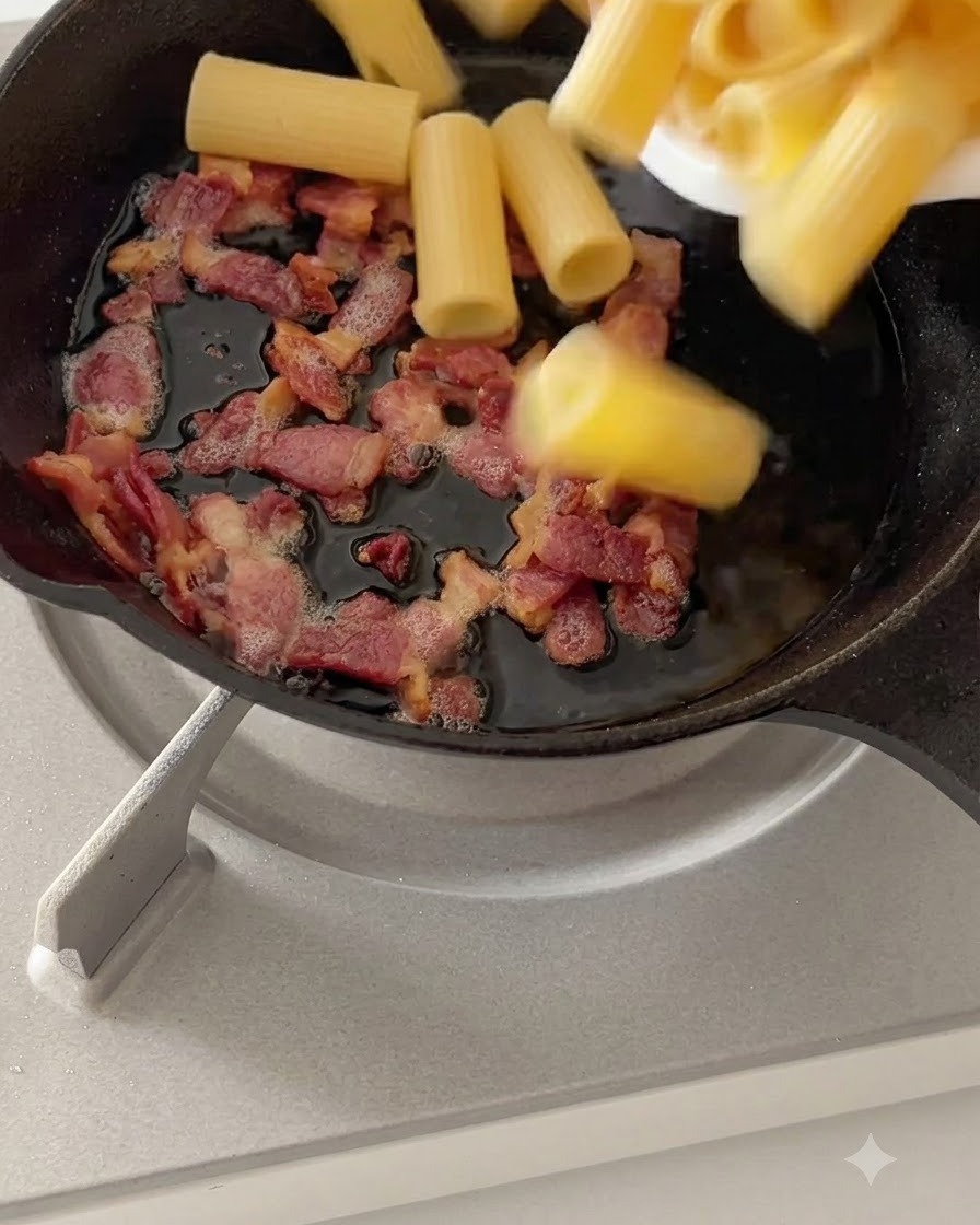 Rigatoni bolliti saltati insieme alla pancetta cotta in una padella a fuoco basso.
