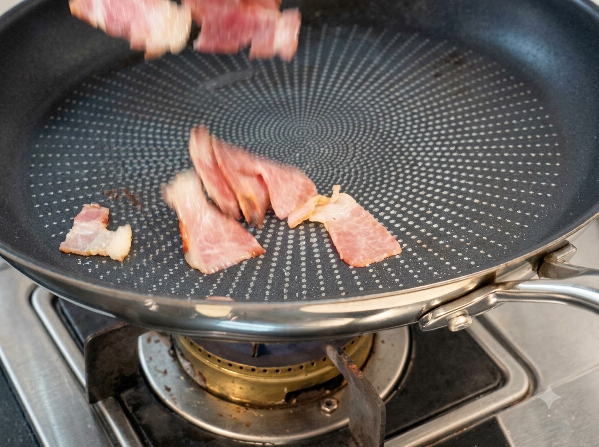 Pezzi di pancetta tagliati a fette messi a cuocere in una padella antiaderente asciutta.