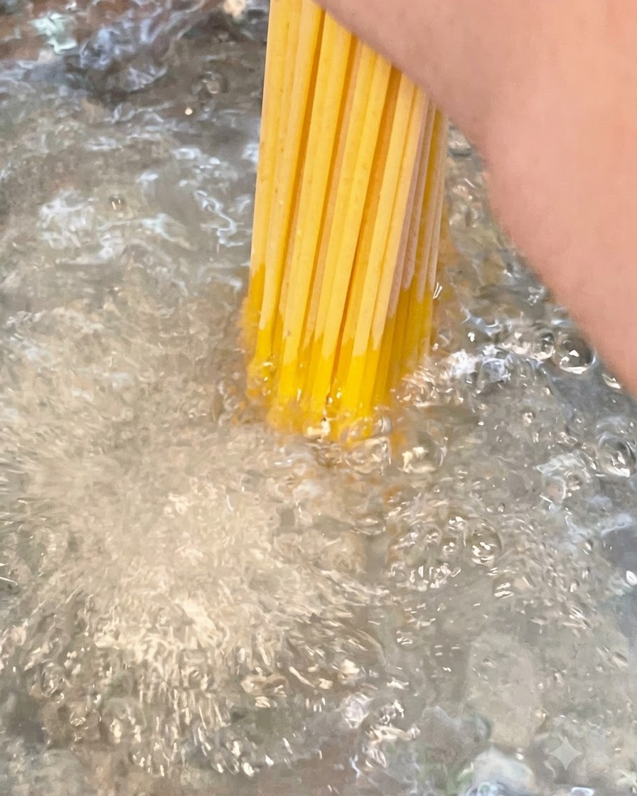Un mazzo di spaghetti lunghi secchi immersi in una pentola di acqua salata in forte ebollizione.