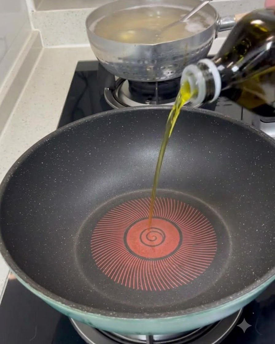 Olio extravergine doliva versato da una bottiglia al centro di una padella scura preriscaldata.