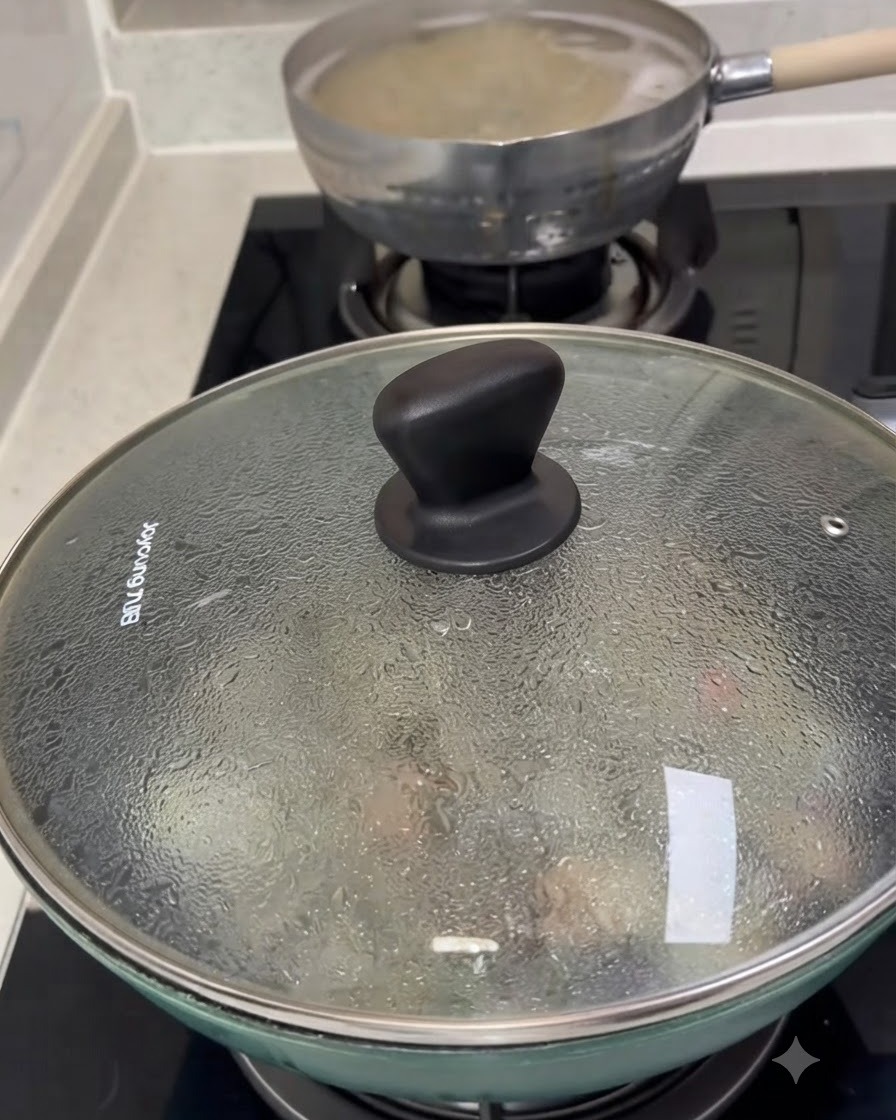 Un coperchio di vetro che copre una padella piena di vongole in cottura, con condensa visibile sulla superficie.