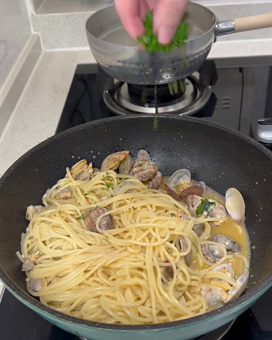 Prezzemolo verde fresco tritato cosparso dallalto su una padella di spaghetti e vongole cotti.
