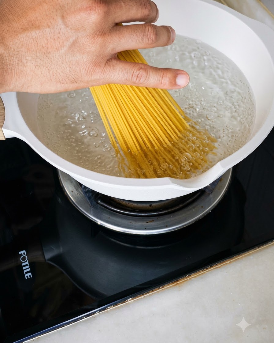 Una manciata di spaghetti crudi calati in una pentola bianca piena di acqua bollente.