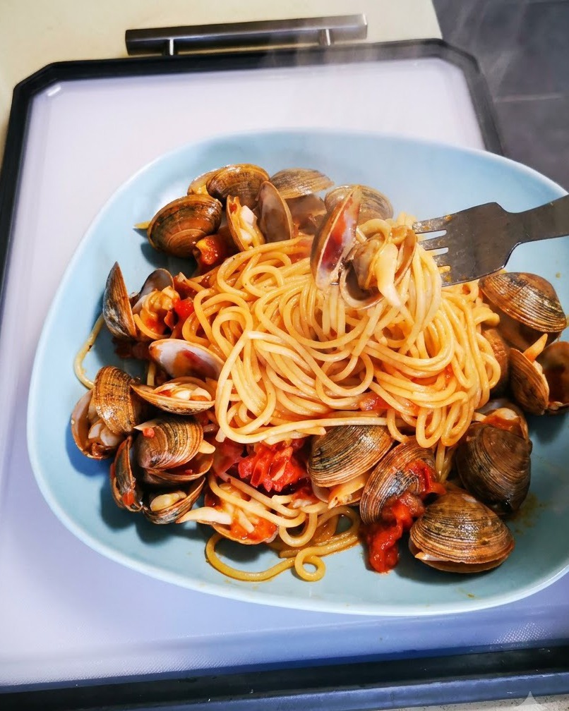 Primo piano di vino bianco versato su vongole fresche e pomodorini in una padella.