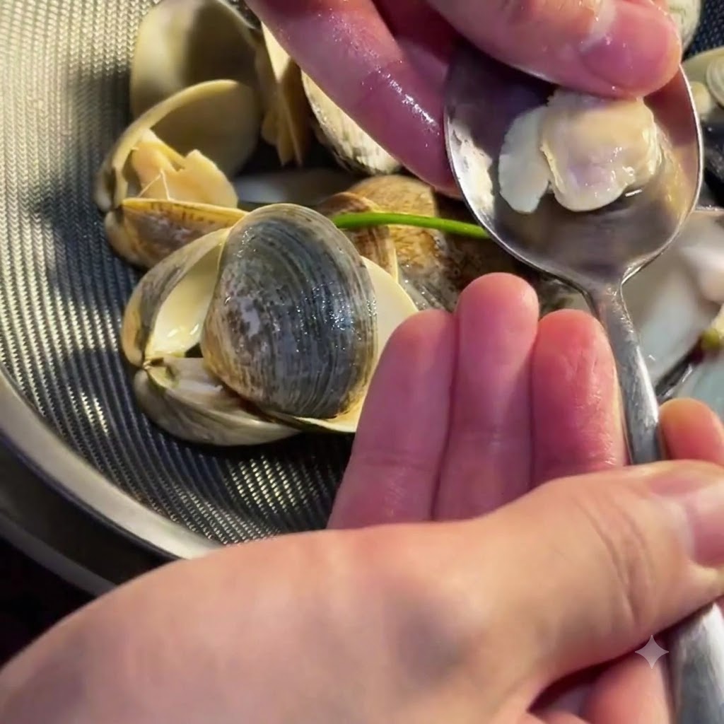 Una persona che utilizza un cucchiaino per estrarre la tenera polpa delle vongole dal guscio.