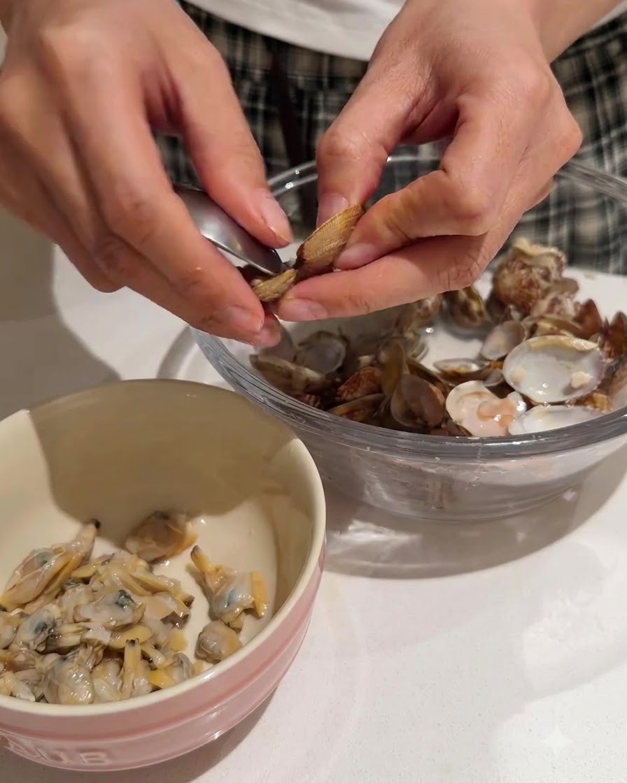 Mani che estraggono la tenera carne di vongola dai gusci in una ciotola dal bordo rosa.