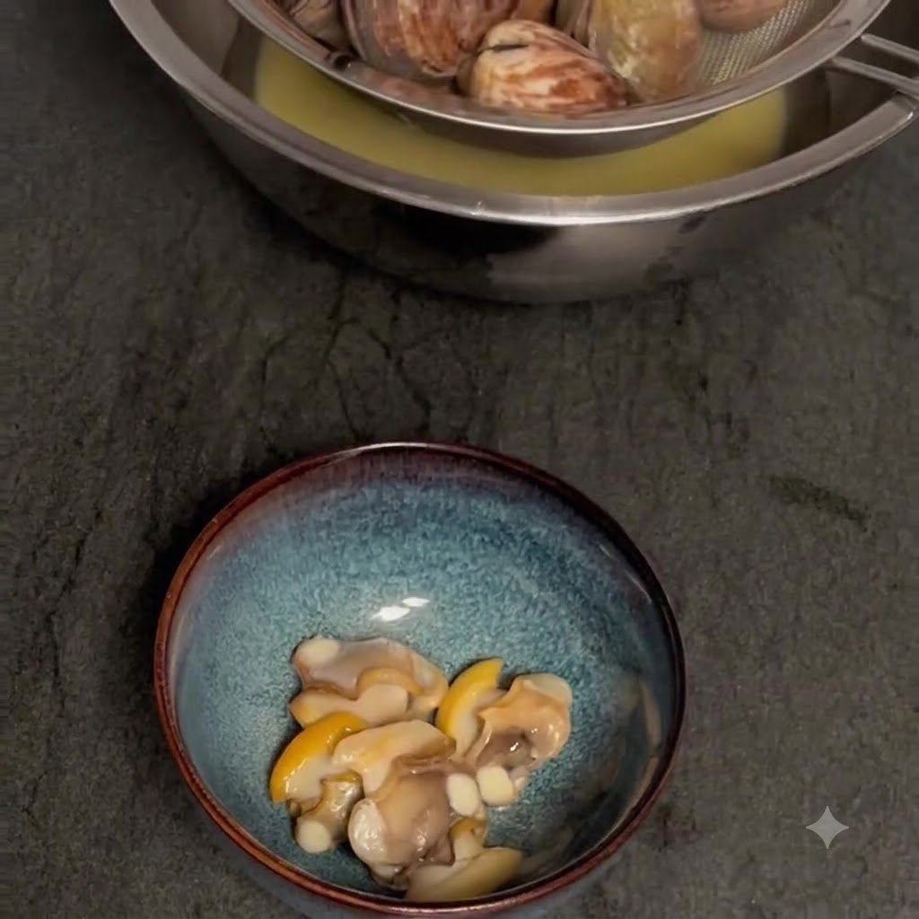 Vongole cotte filtrate sopra una ciotola per raccogliere il brodo, con la polpa sgusciata a parte.