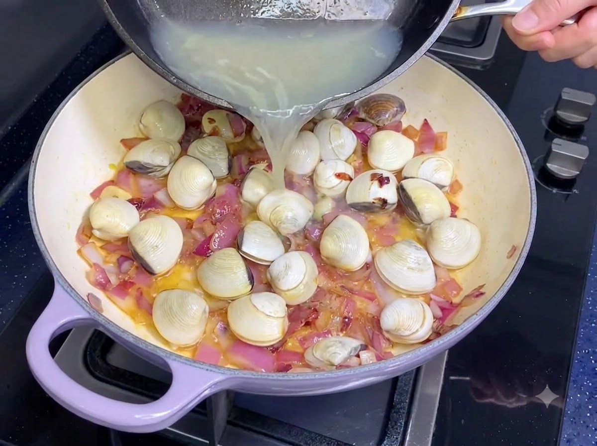 Brodo di vongole versato da una padella in una padella con cipolle e aglio.