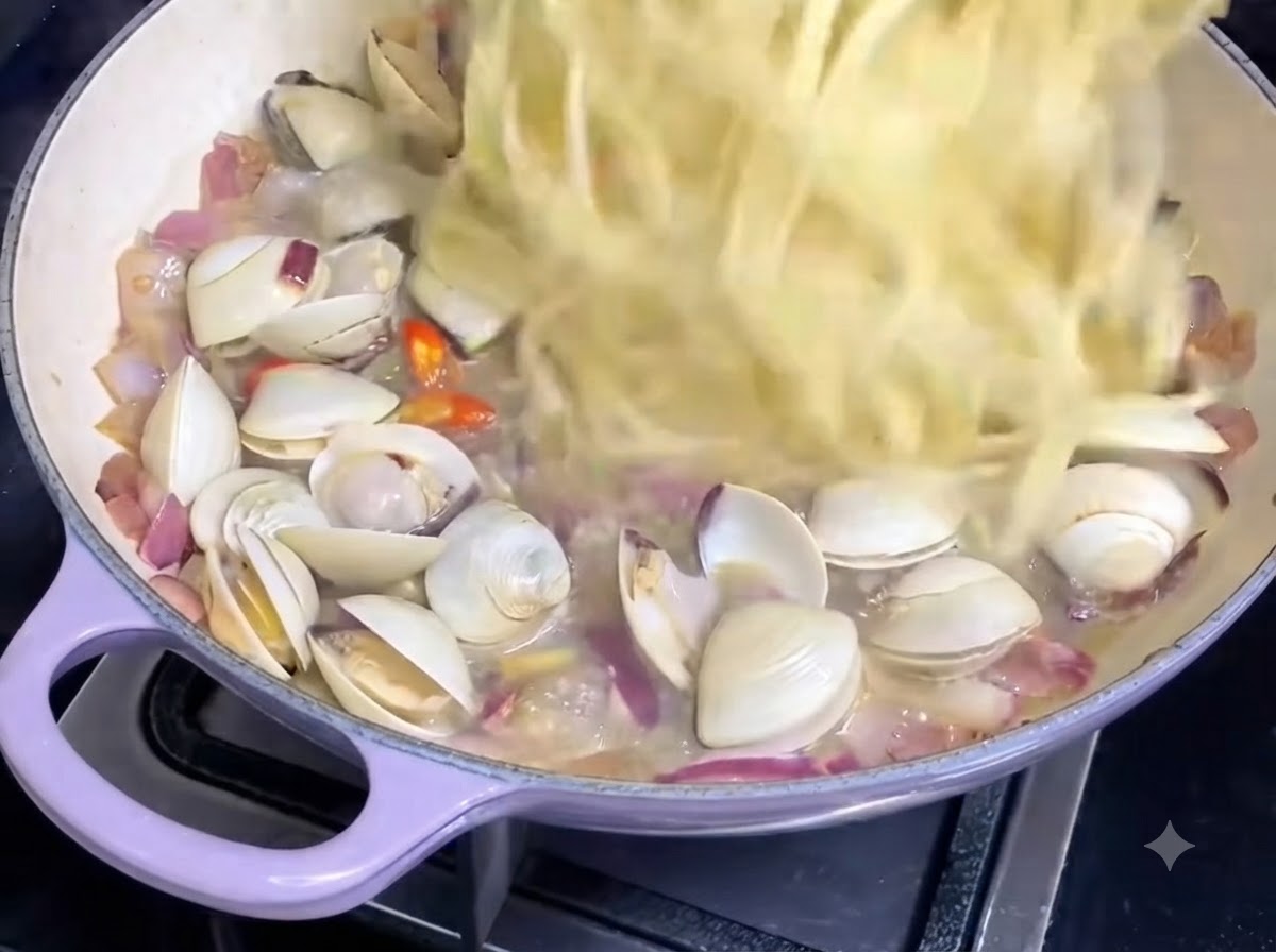 Fili di spaghetti cotti trasferiti in una padella contenente salsa di vongole e cipolle.