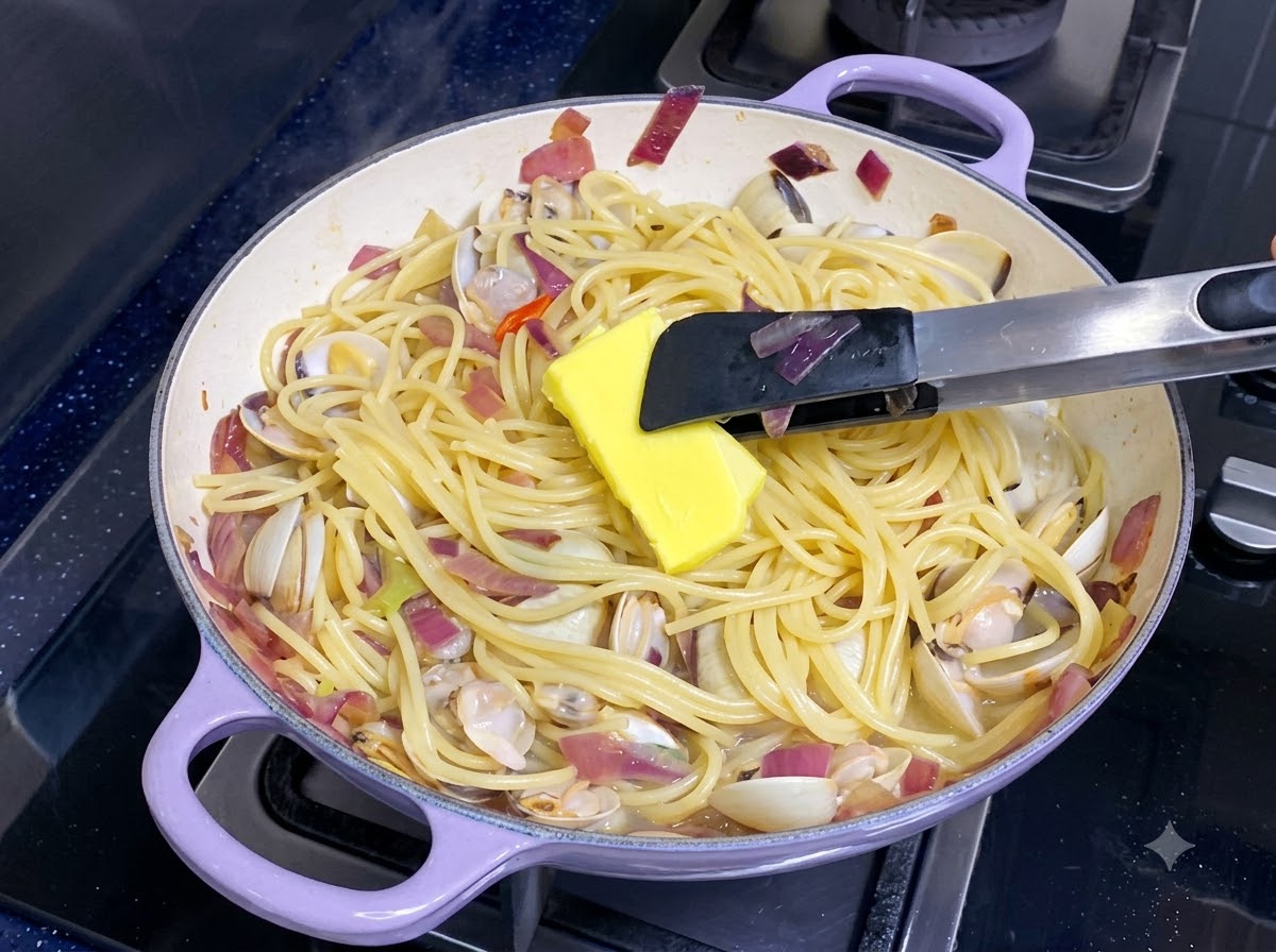 Una noce di burro giallo che si scioglie in una padella di spaghetti misti e vongole.