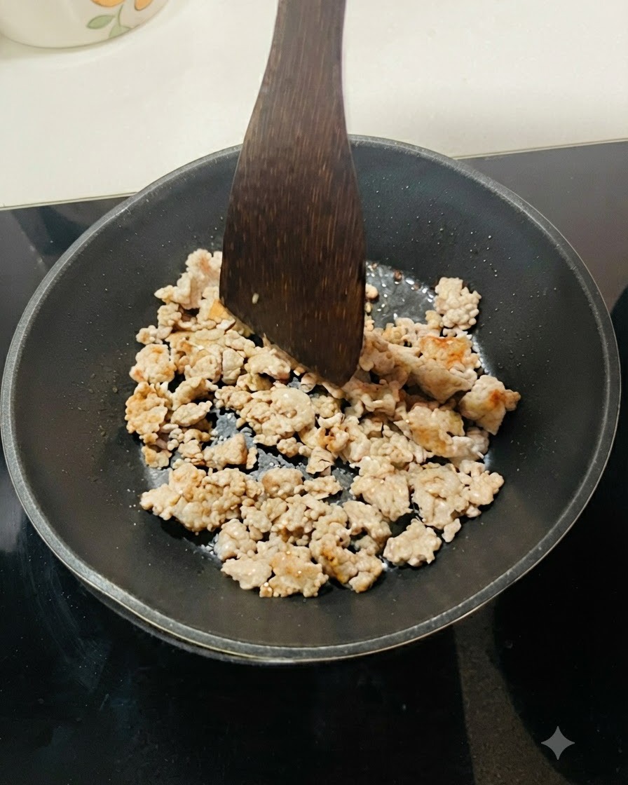 Carne macinata in cottura in una padella nera, separata in piccoli pezzi con una spatola di legno.