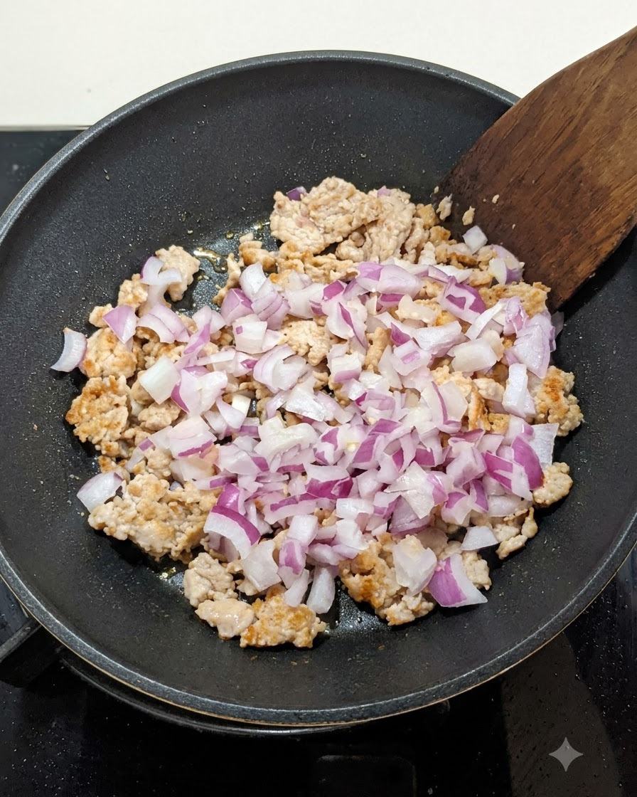Cipolle rosse a dadini mescolate alla carne macinata rosolata in una padella, mentre vengono girate con una spatola di legno.
