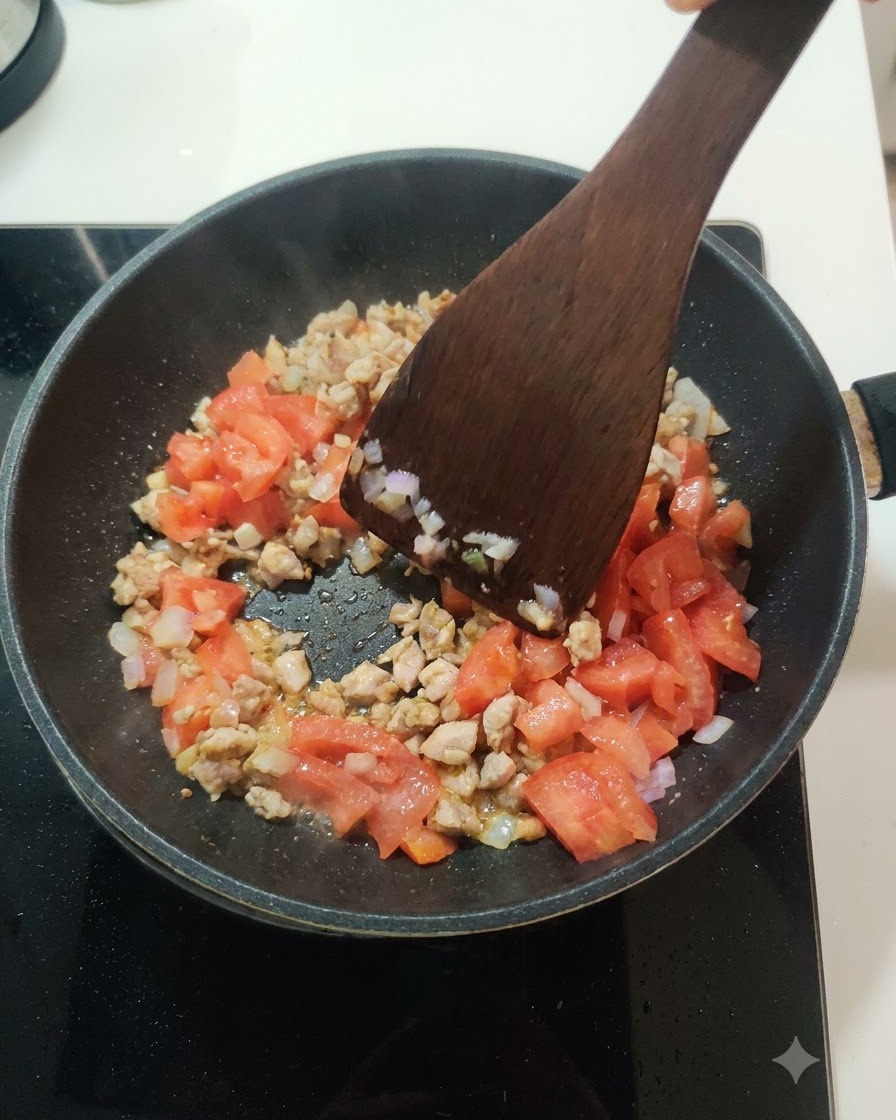 Pomodori freschi a dadini mescolati al composto di carne e cipolla allinterno di una padella.