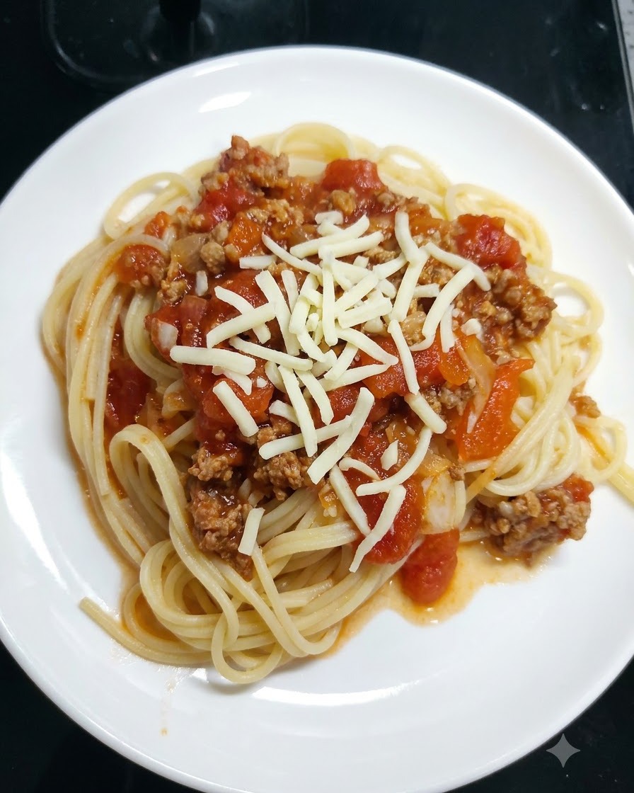 Mozzarella grattugiata cosparsa sopra gli spaghetti coperti di sugo di pomodoro in un piatto bianco.