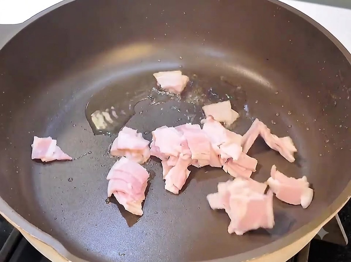 Pezzi di pancetta che sfrigolano e cuociono in una padella nera sul fuoco.