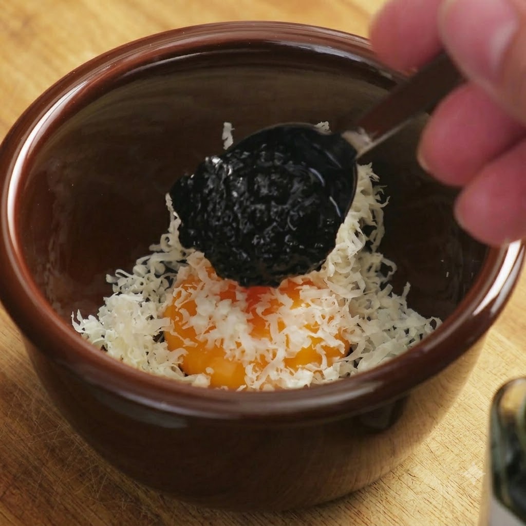 Una cucchiaiata scura di salsa al tartufo nero che viene fatta cadere sulla miscela di tuorlo duovo e formaggio.