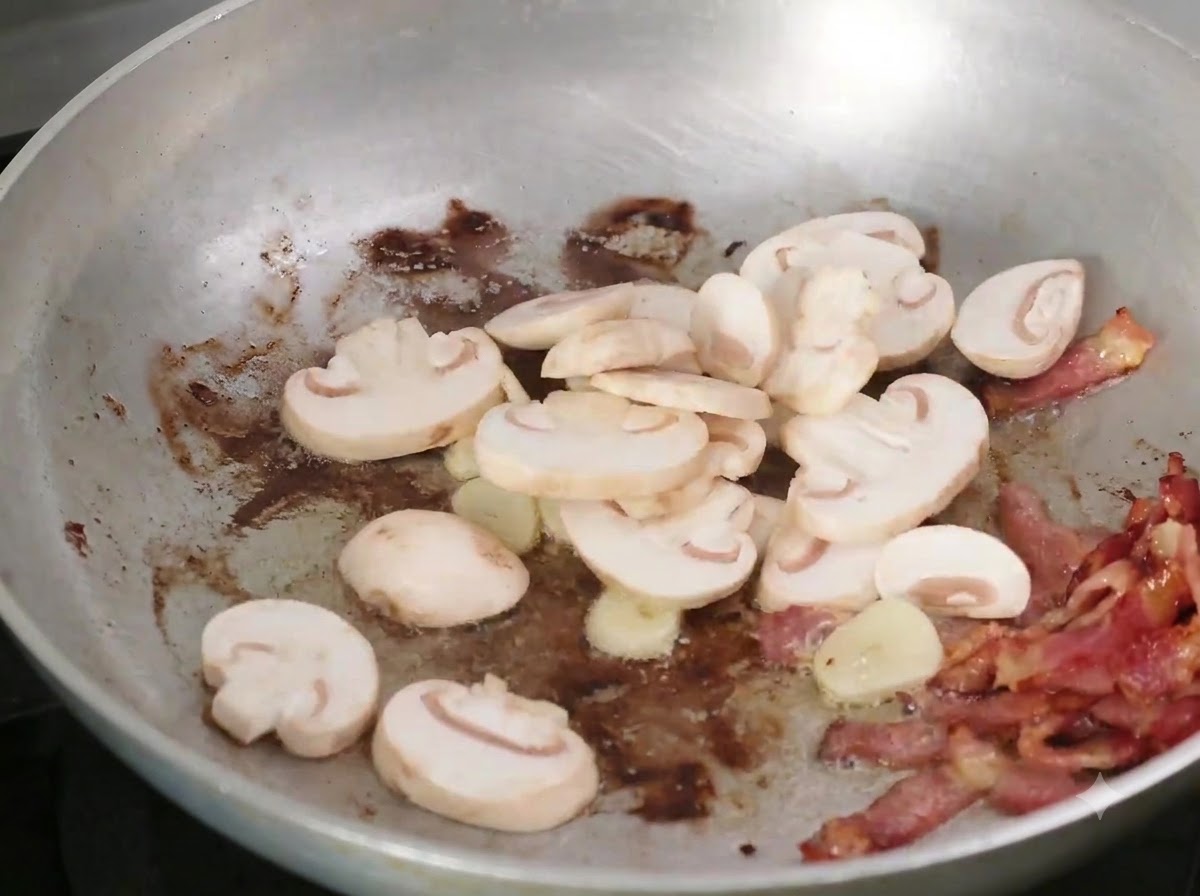 Funghi affettati aggiunti alla padella con pancetta e aglio.