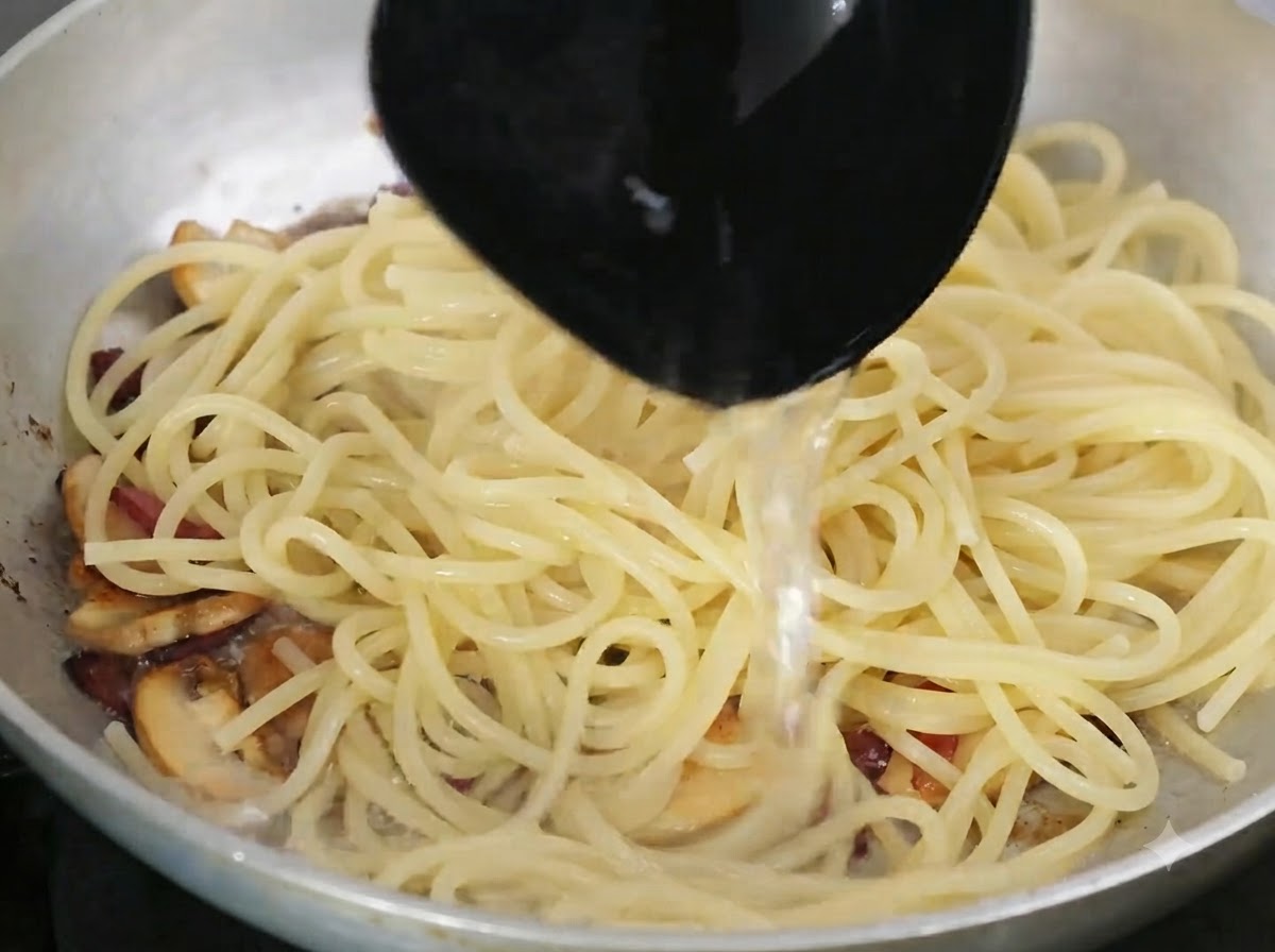 Un mestolo che versa lacqua di cottura ricca di amido nella padella contenente la pasta e gli ingredienti.