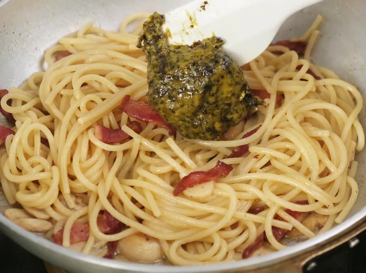 Salsa al tartufo nero aggiunta con un cucchiaio in una padella di pasta cotta e pancetta.