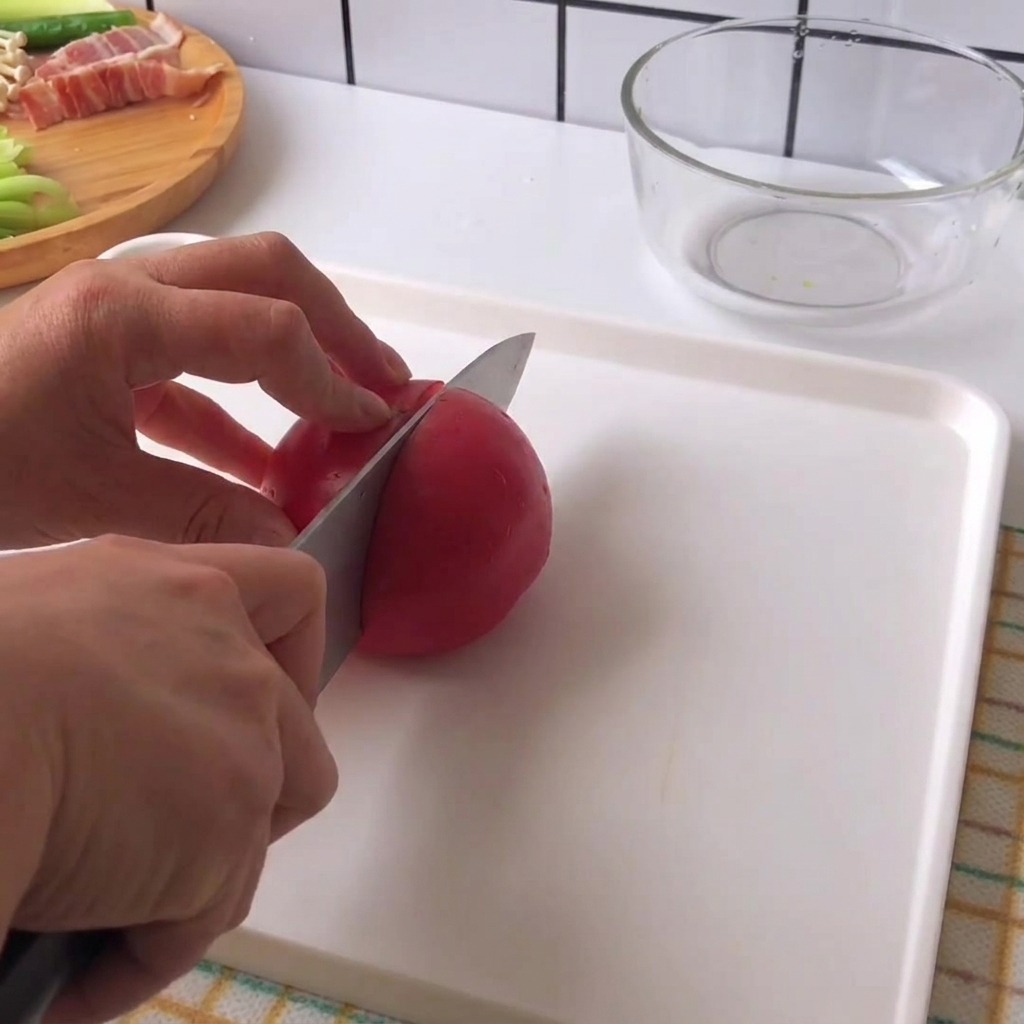 Mani che tengono un coltello e tagliano un pomodoro rosso fresco a pezzi su un tagliere bianco.