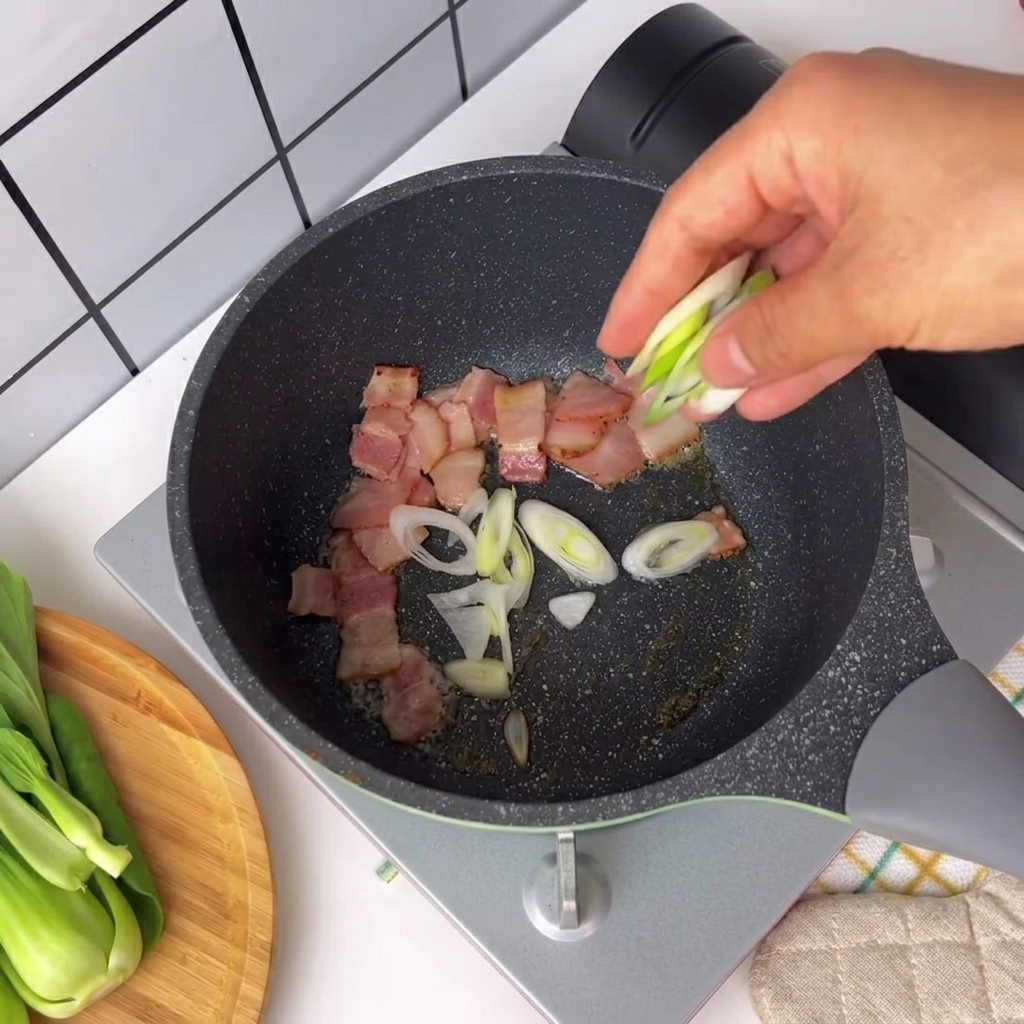 Cipollotti tritati e peperoncino cosparsi in una padella con pezzi di pancetta sfrigolanti.