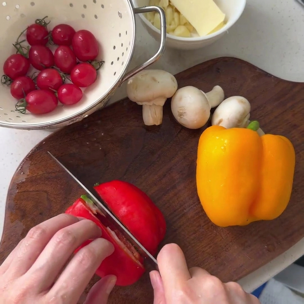 Un peperone rosso affettato su un tagliere di legno accanto a un peperone giallo e funghi champignon.