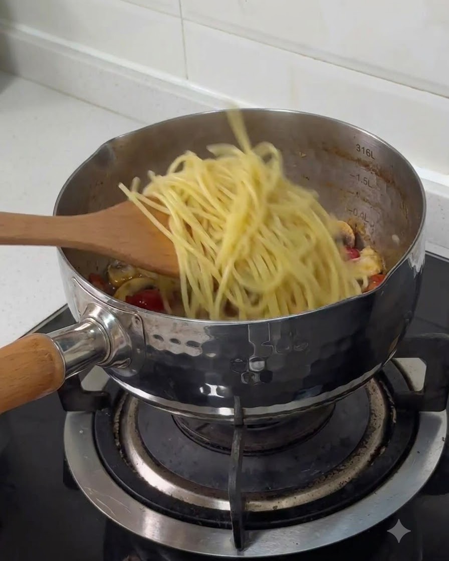 Spaghetti lessati trasferiti con una spatola di legno in una pentola di acciaio inossidabile con gli altri ingredienti cotti.