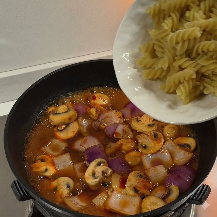 Pasta fusilli bollita versata da un piatto bianco in una padella piena di salsa e verdure in ebollizione.