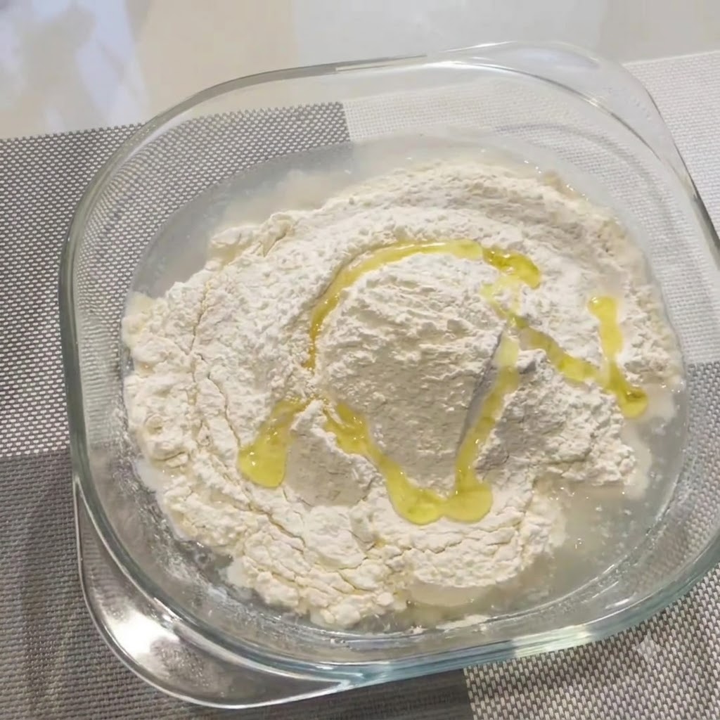 Olio doliva versato a filo sulla farina e sullacqua in una ciotola di vetro.
