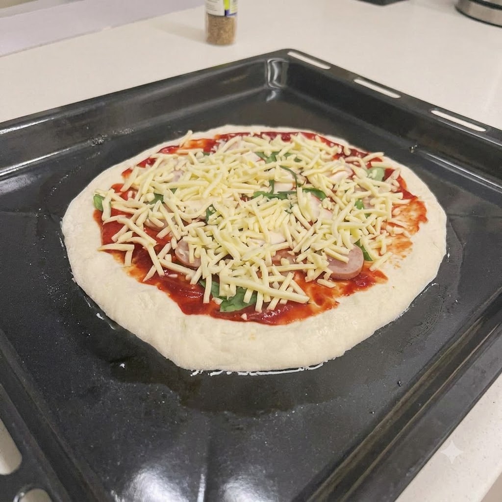 Una pizza cruda guarnita con salsa rossa, fette di insaccato, basilico fresco e formaggio grattugiato su una teglia nera.